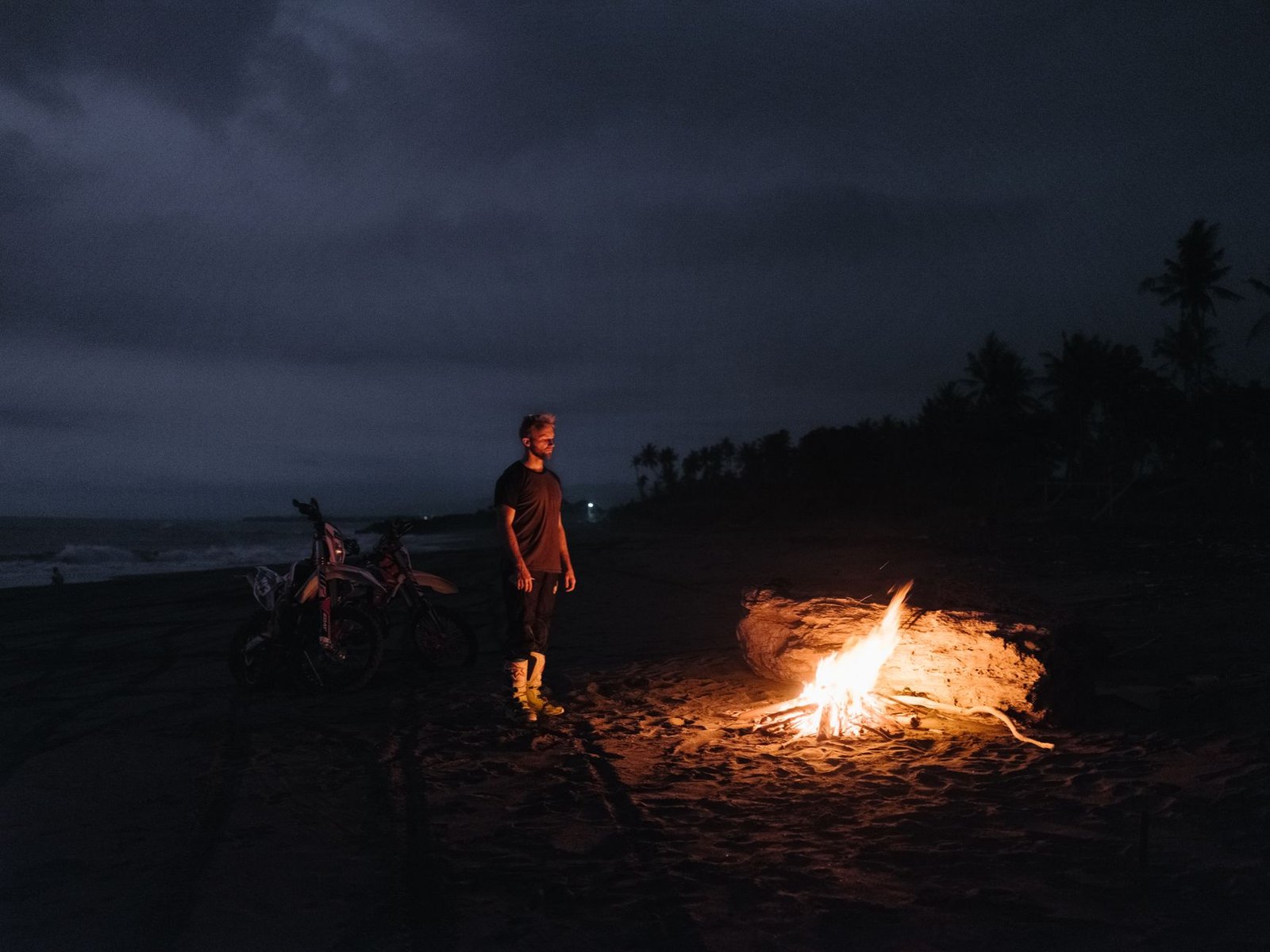 Hoguera encendida en una playa durante la noche con gente alrededor