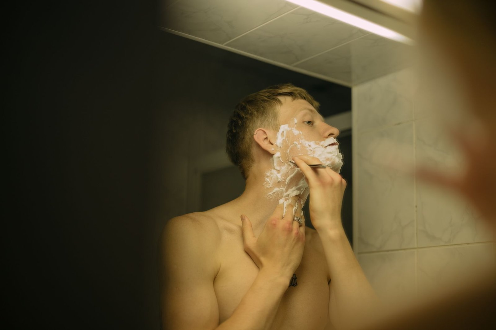 Hombre afeitándose frente al espejo del baño con espuma en la cara